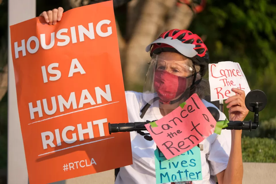 Elderly woman wearing Covid mask holding up "Housing is a human right" sign during tenants' rights protest